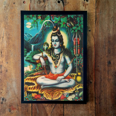 Quadro emoldurado com pintura de Shiva sentado em meditação, com tridente na mão e serpente ao pescoço, sobre fundo de folhagem verde.
