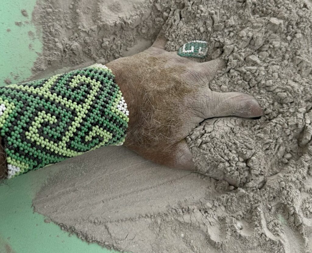 Mão com grafismo kene sobre uma porção de rapé em pó