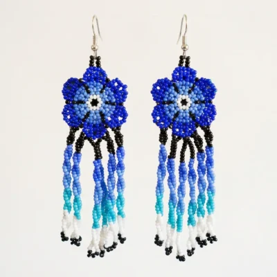 Par de brincos indígenas de missangas em flor azul com franjas longas em degradê do azul ao branco, suspensos lado a lado sobre fundo claro.