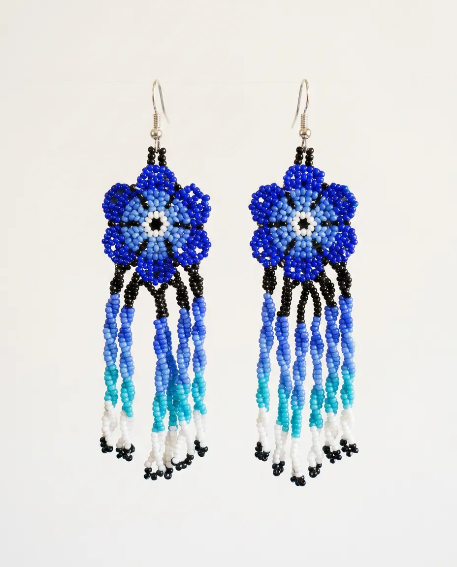Par de brincos indígenas de missangas em flor azul com franjas longas em degradê do azul ao branco, suspensos lado a lado sobre fundo claro.