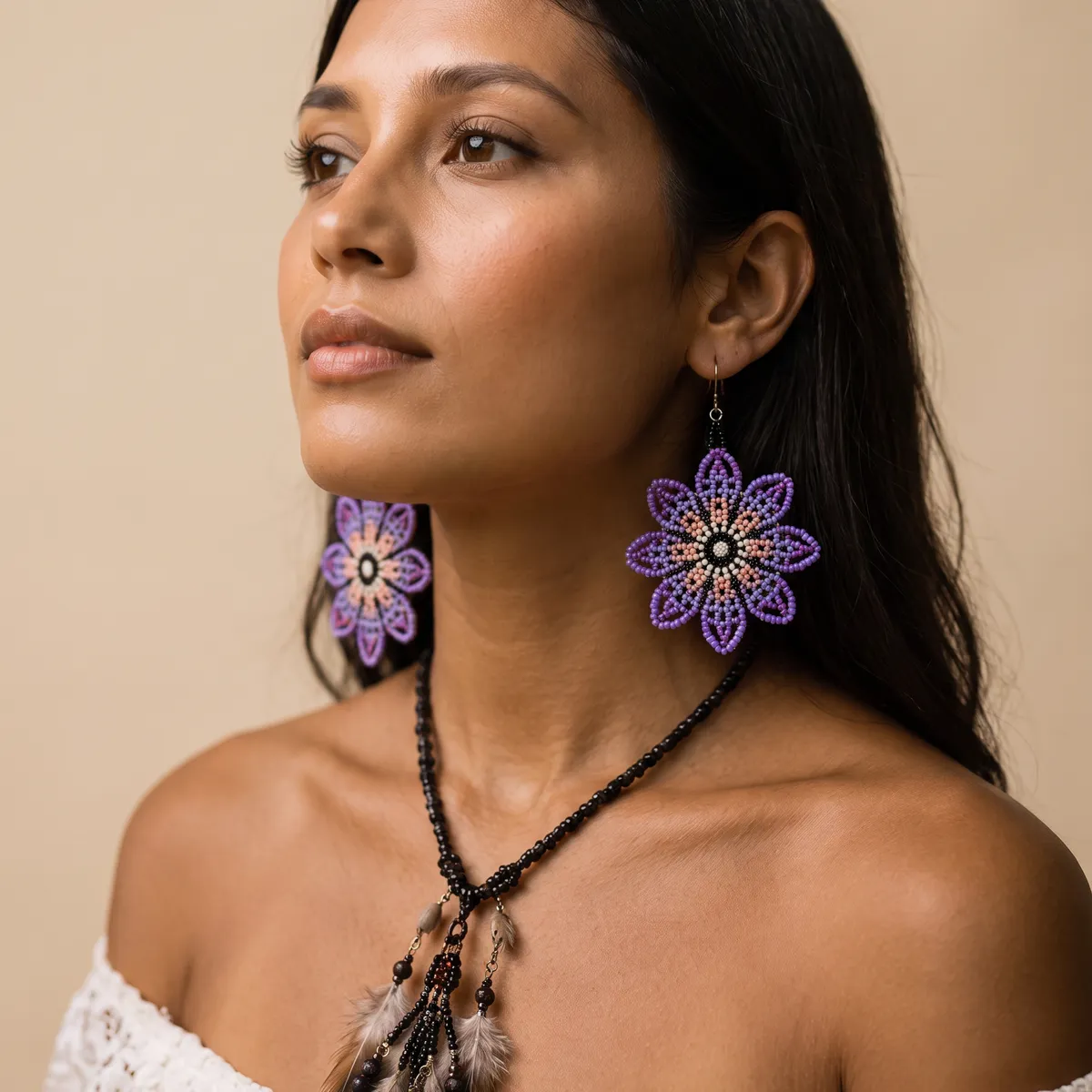 Mulher usando um par de brincos indígenas de missangas em flor roxa e lilás com pétalas em pêssego e branco.