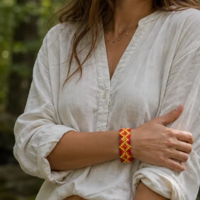Pulseira indígena de miçanga elástica laranja e amarela fina, padrão zigue-zague, usada no pulso em ambiente de floresta