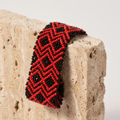 Pulseira indígena de miçanga elástica Red Snake média, losangos encadeados em vermelho e preto, apoiada em bloco de travertino