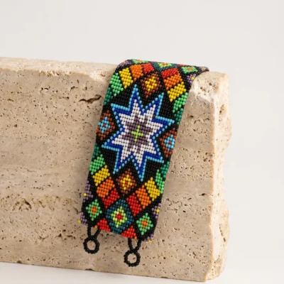 Pulseira indígena de miçanga Wixarica Estrela Cósmica, estrela branca de oito pontas sobre base preta multicolorida, apoiada em bloco de travertino