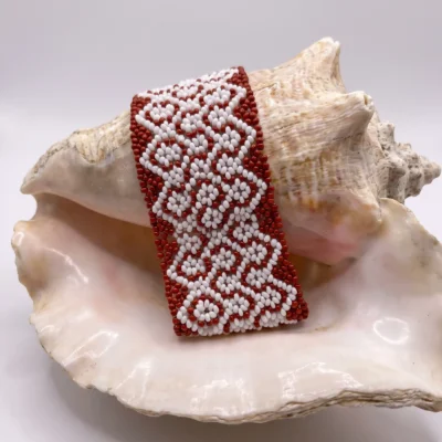 Pulseira indígena Wixarica de miçanga marrom e branca média, padrão grego em terracota, apoiada sobre concha do mar