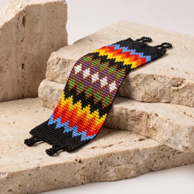 Pulseira indígena Wixarica de miçanga Spanding Universe, faixas em arco-íris sobre base preta com fileira de losangos brancos, apoiada em degraus de travertino